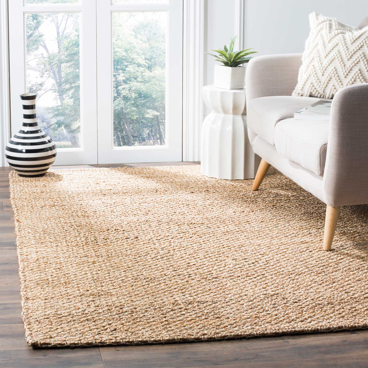 A warm tan jute-and-cotton rug adds quiet texture to a light-filled sitting area.