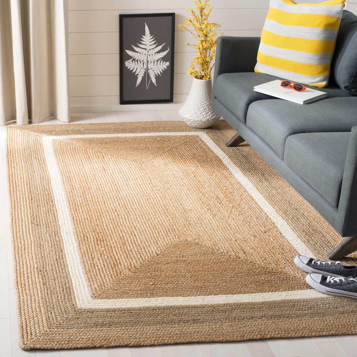 A natural tan rug with ivory and gray borders defines the space beside a charcoal sofa.