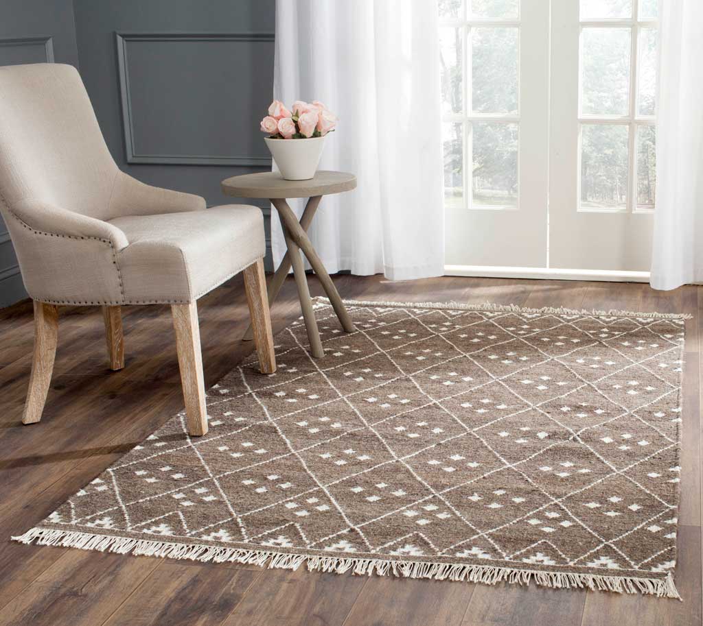 A brown rug with ivory diamond lines and fringe lends warmth beneath a pale armchair.