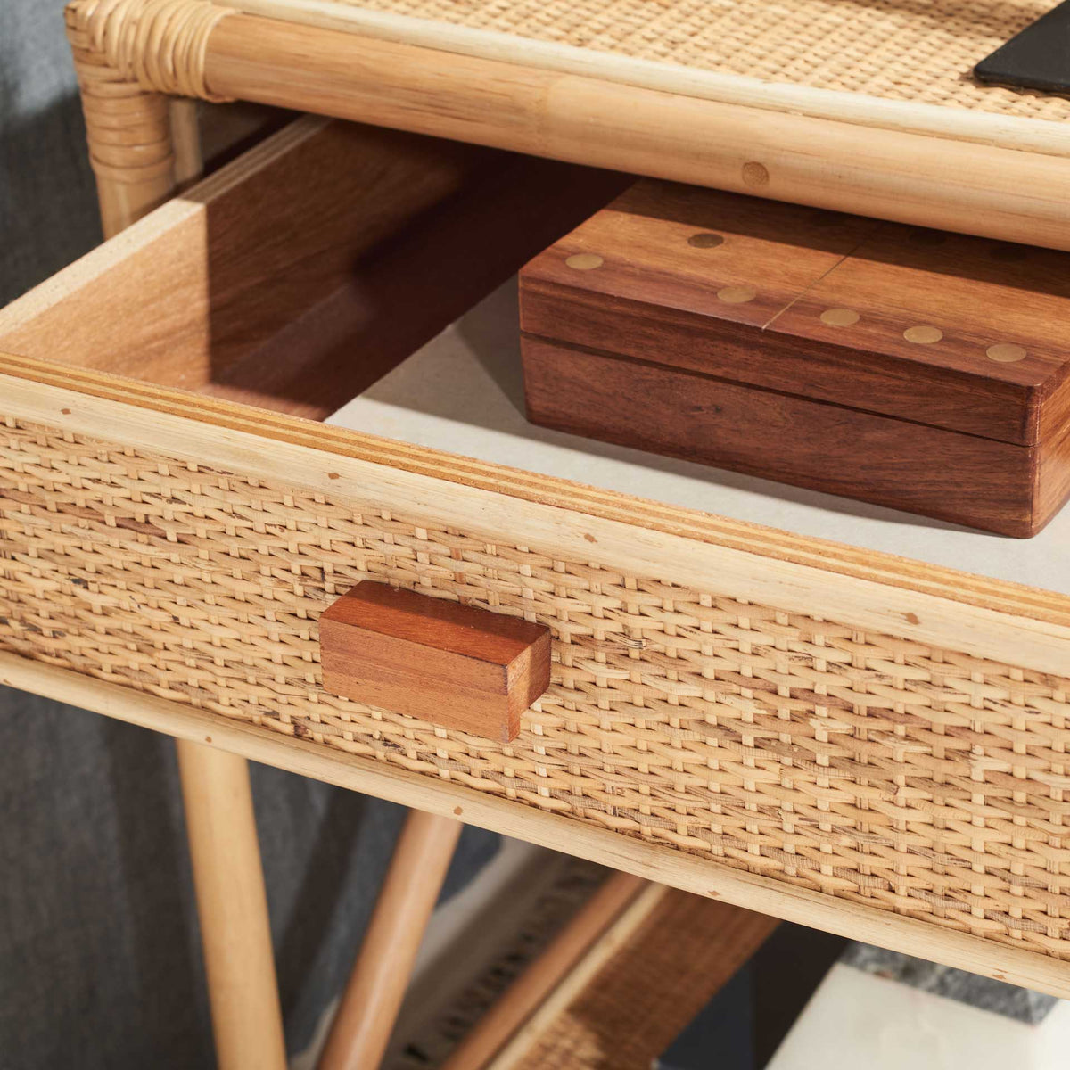 An open, wood-lined drawer holds small essentials behind a woven cane front