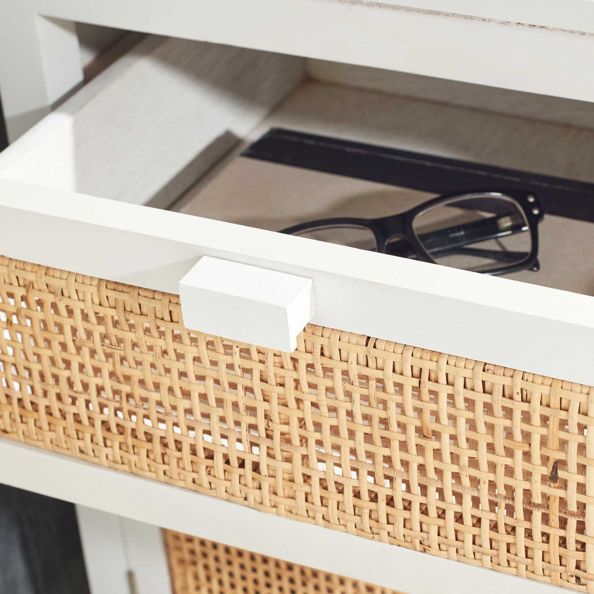 An open white drawer keeps eyeglasses close at hand behind a woven cane front.