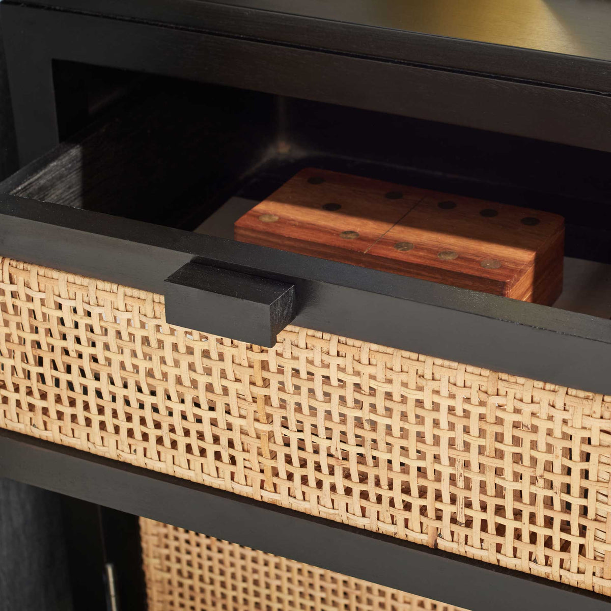 An open black-framed drawer keeps small bedside items behind woven cane.