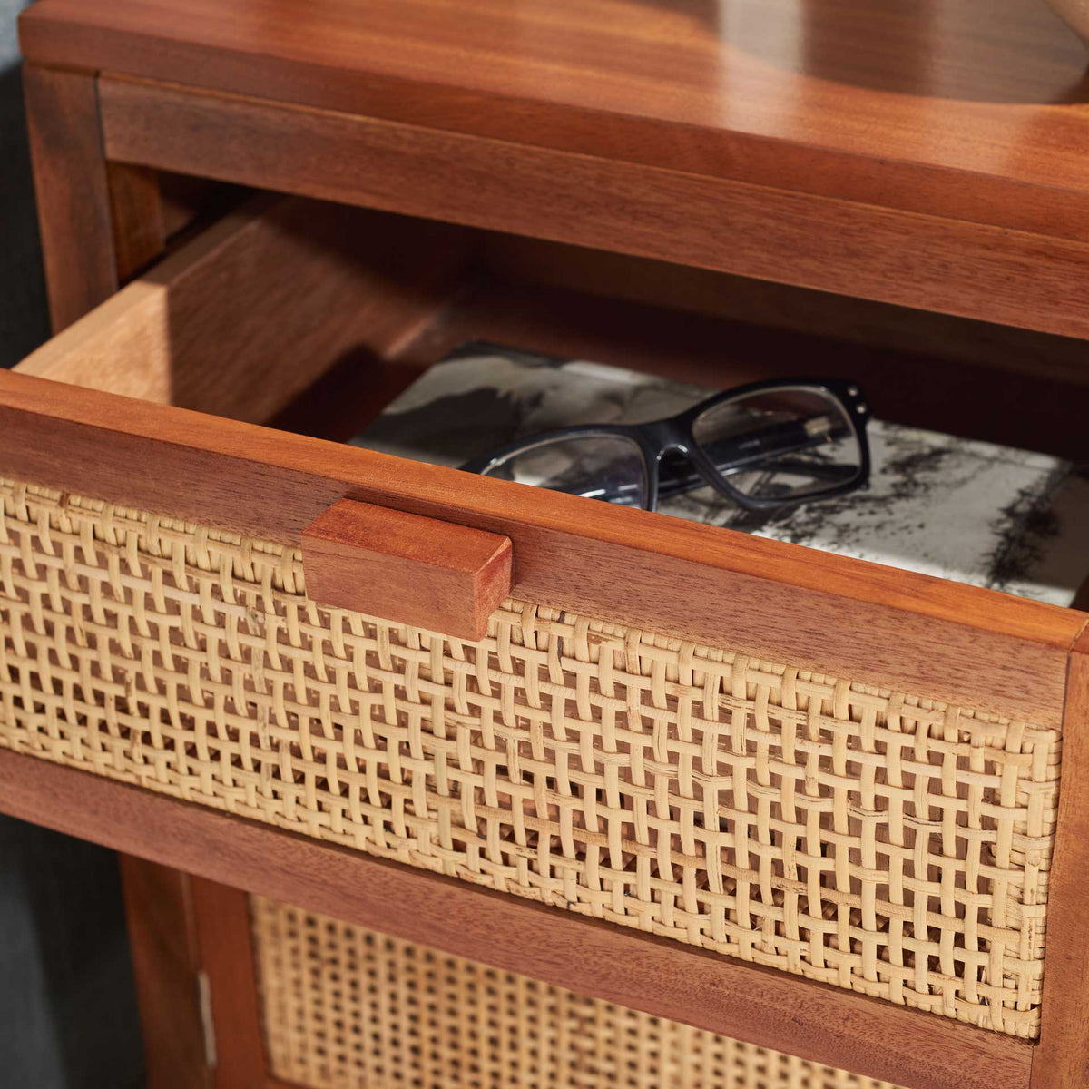 An open woven cane drawer keeps eyeglasses close in a warm wood nightstand