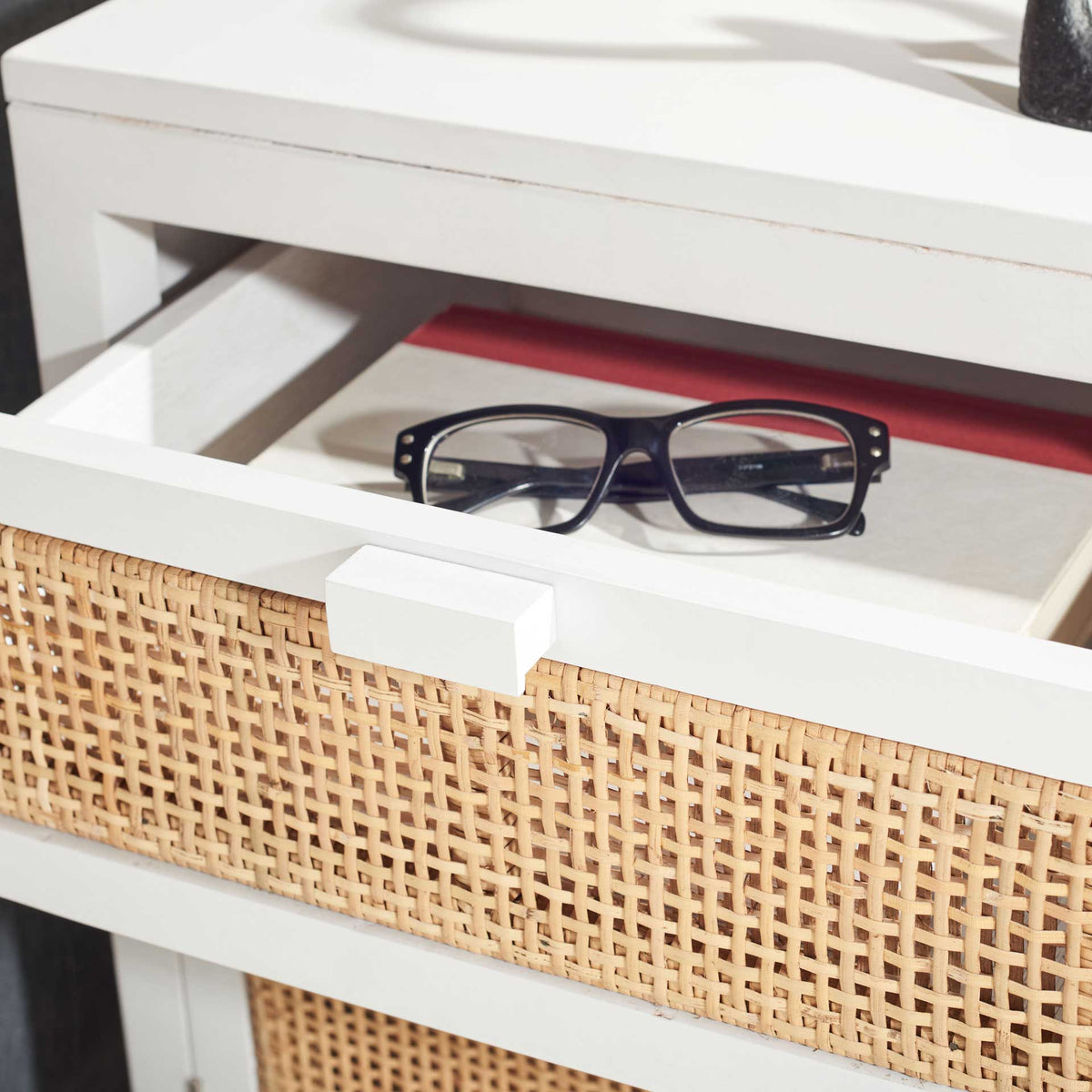 Open white drawer holds eyeglasses above its woven cane front