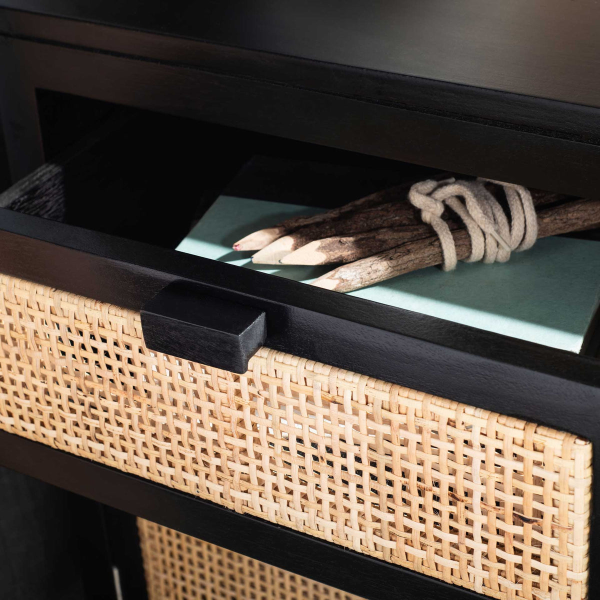 An open cane-front drawer keeps bedside essentials close in a black nightstand