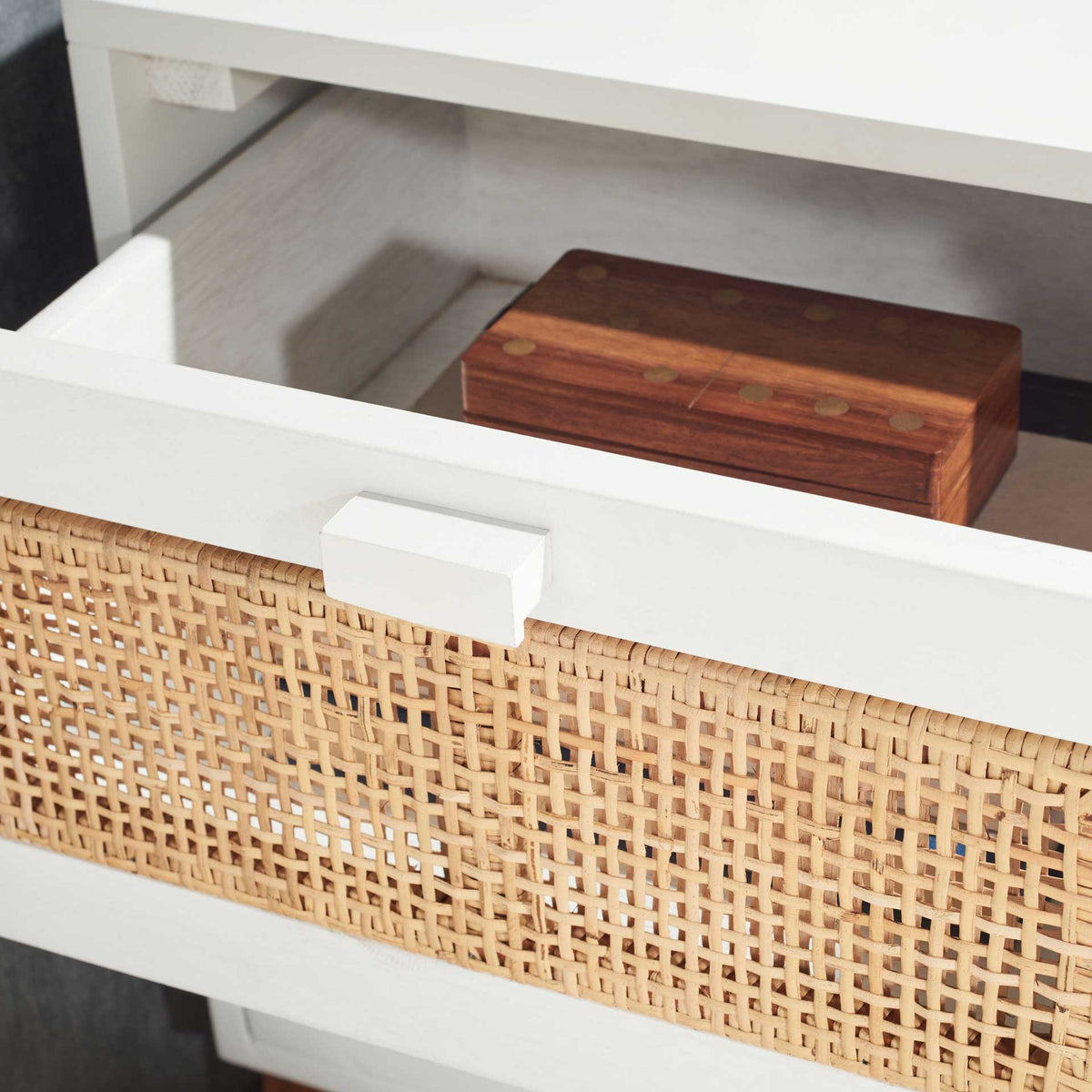 An open woven cane drawer holds small essentials inside the white nightstand.