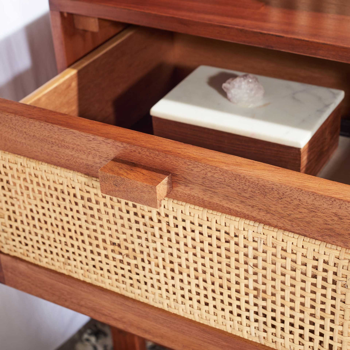 An open cane-front drawer holds small items inside a warm wood storage compartment.
