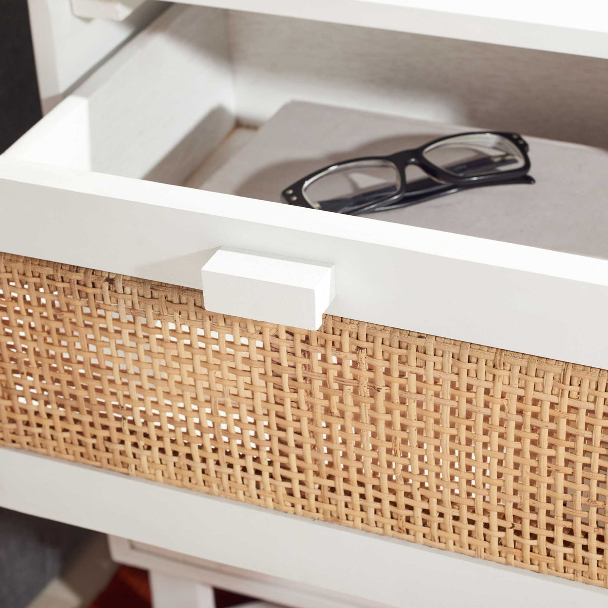 An open cane-front drawer keeps eyeglasses within reach inside the white nightstand.