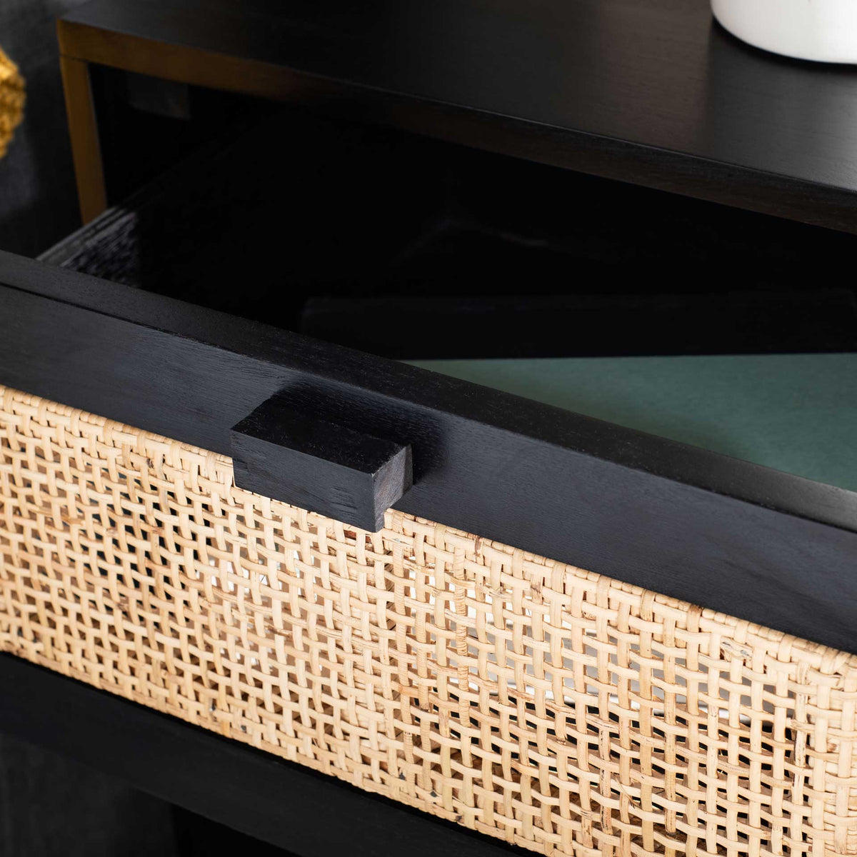 An open cane-front drawer reveals accessible storage beneath the black tabletop.