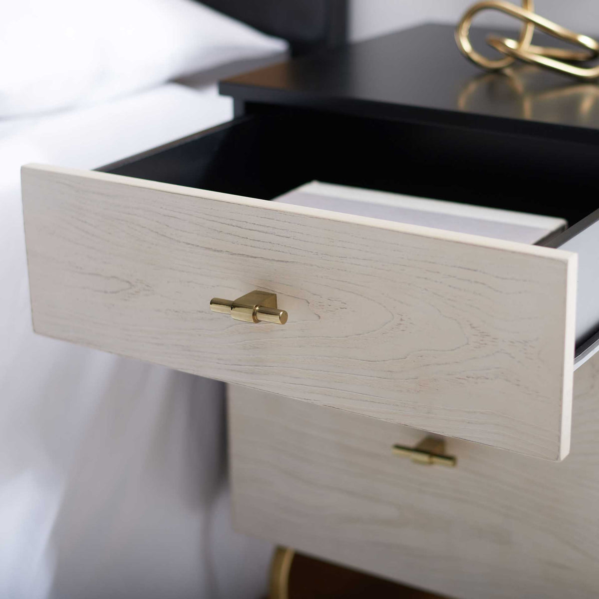 The upper whitewashed drawer opens to a dark compartment for bedside essentials.