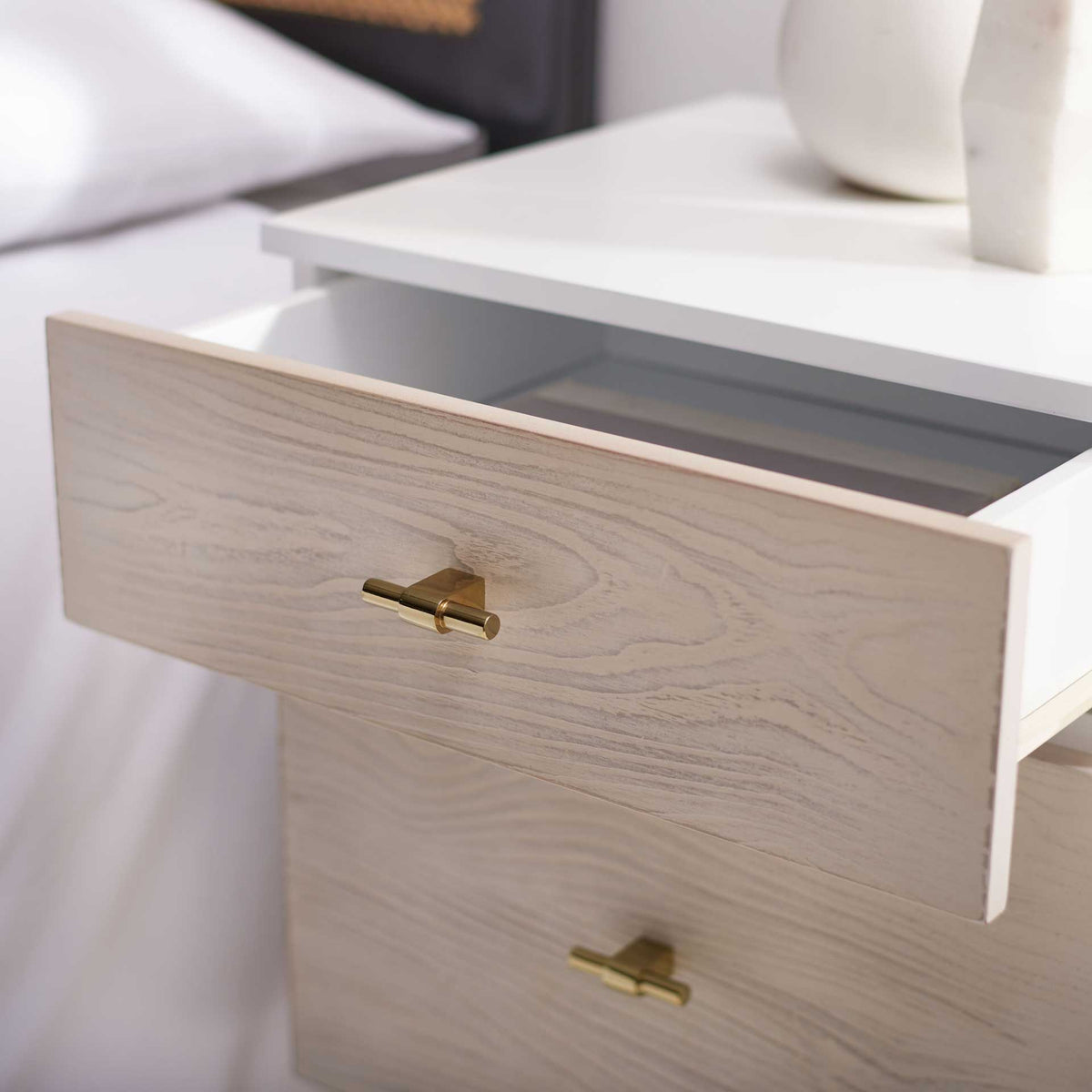 A whitewashed upper drawer opens to a light-toned compartment for everyday bedside essentials.