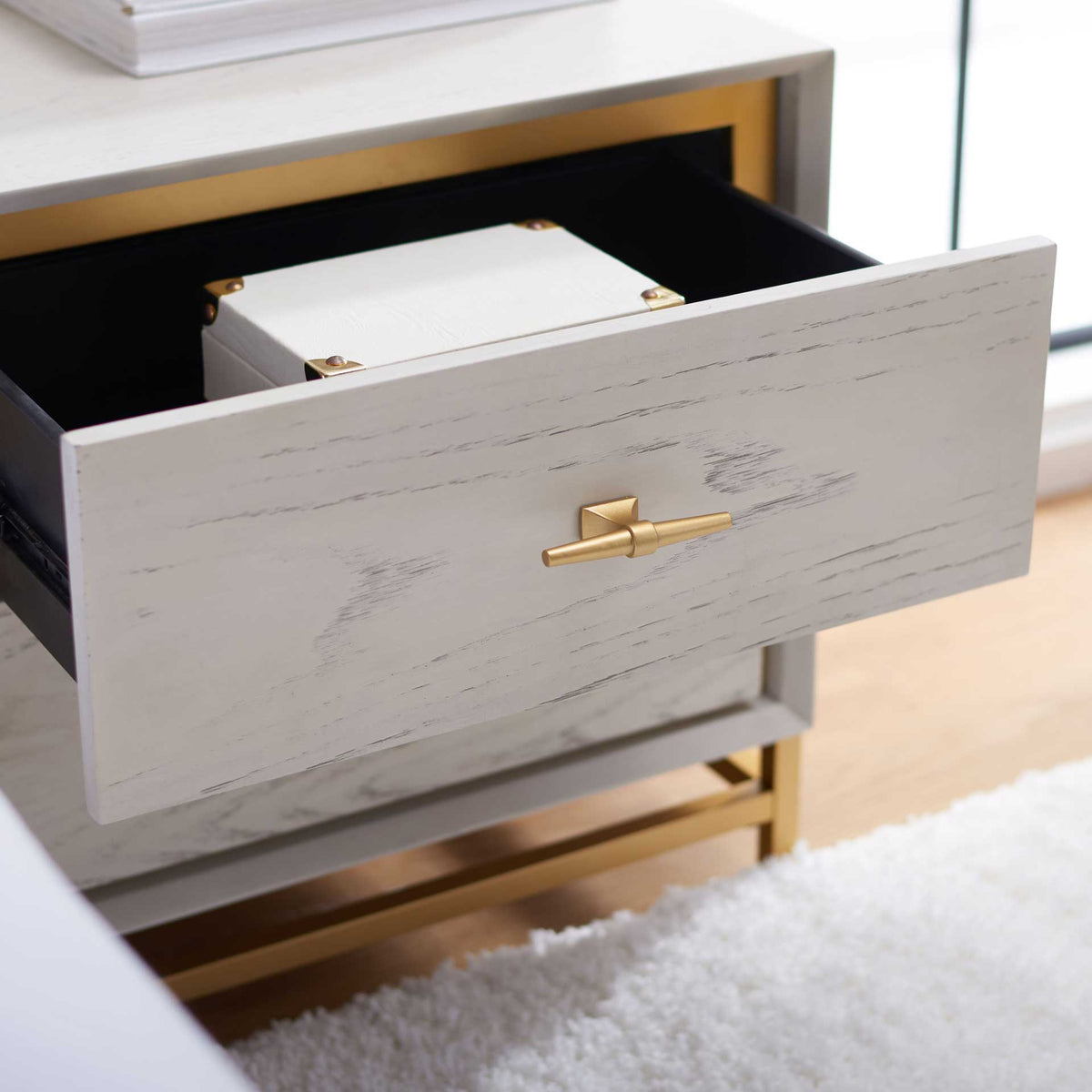 An open upper drawer reveals bedside storage behind a whitewashed front and brass T-bar pull