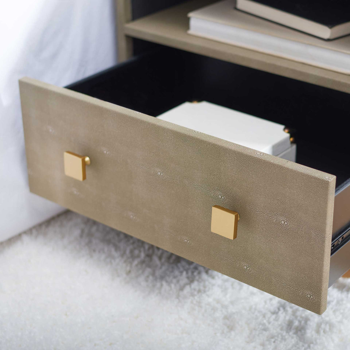 An open drawer reveals a dark storage interior behind a pebbled taupe front with square brass-tone pulls