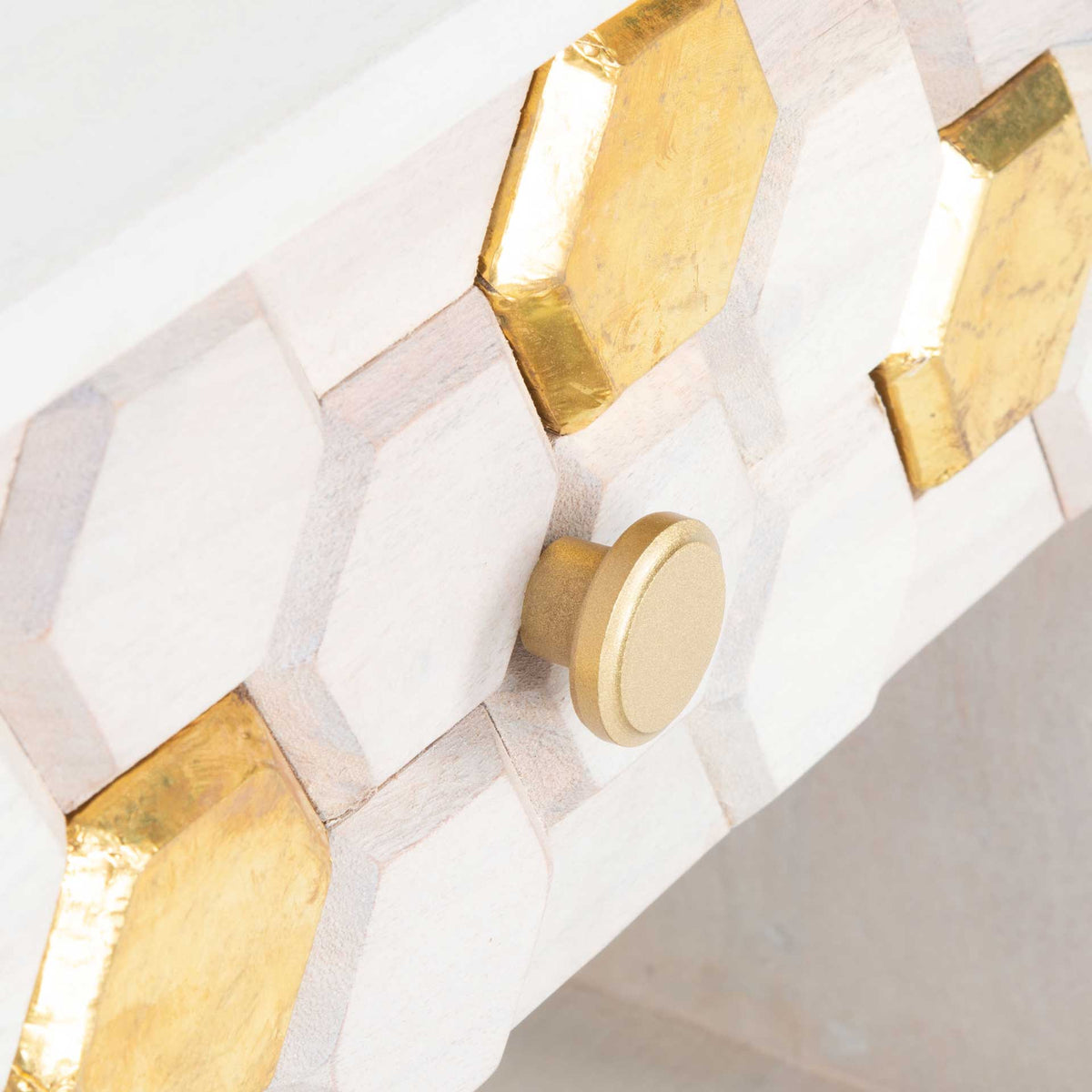 Round brass-tone knob and metallic hexagon accents bring warmth to the whitewashed drawer front.