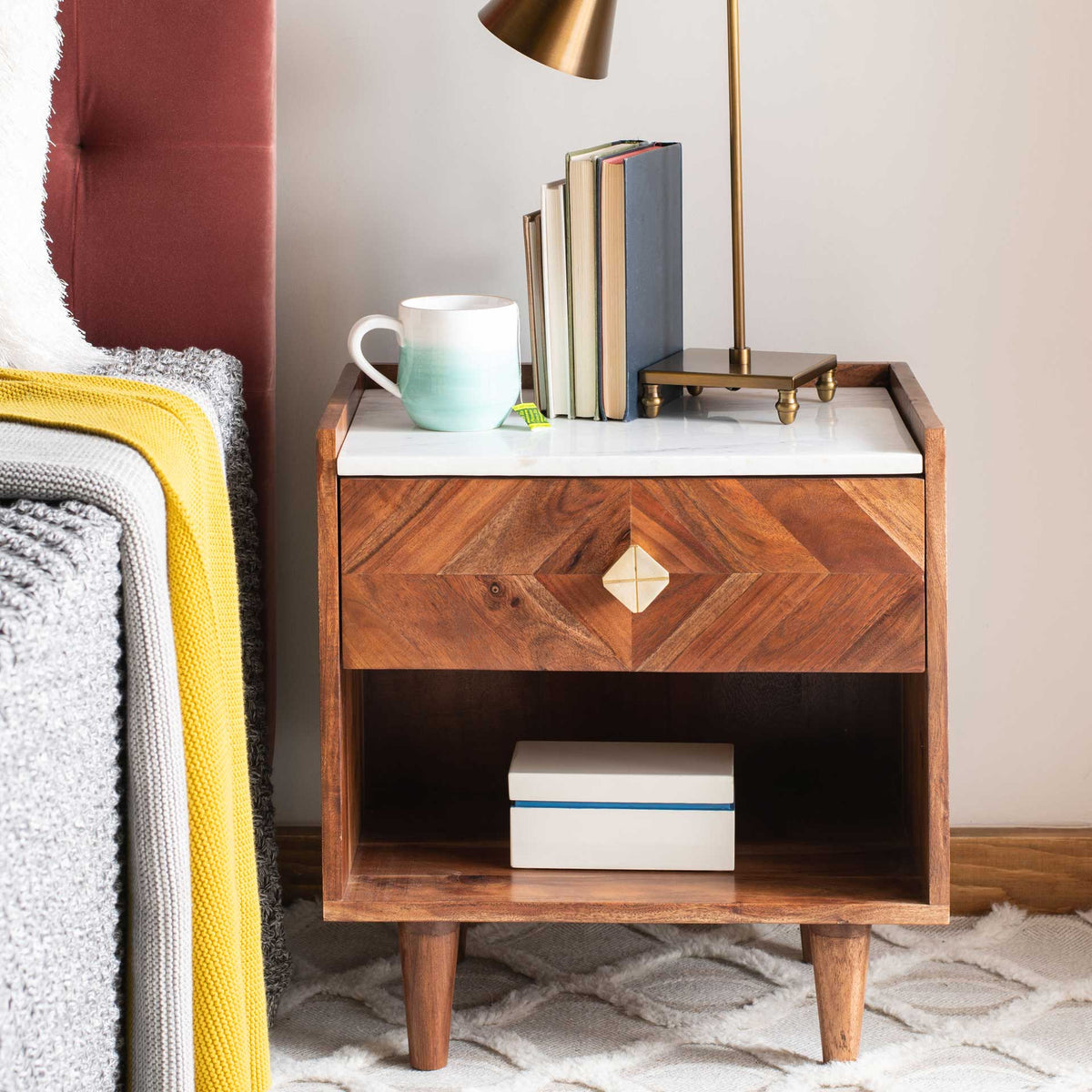 A warm wood drawer with geometric grain and a gold-toned knob sits above an open shelf for bedside essentials.
