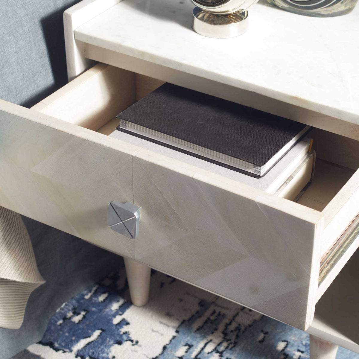 A pullout drawer keeps books close at hand beneath the marble-look top, with a geometric silver-toned knob.
