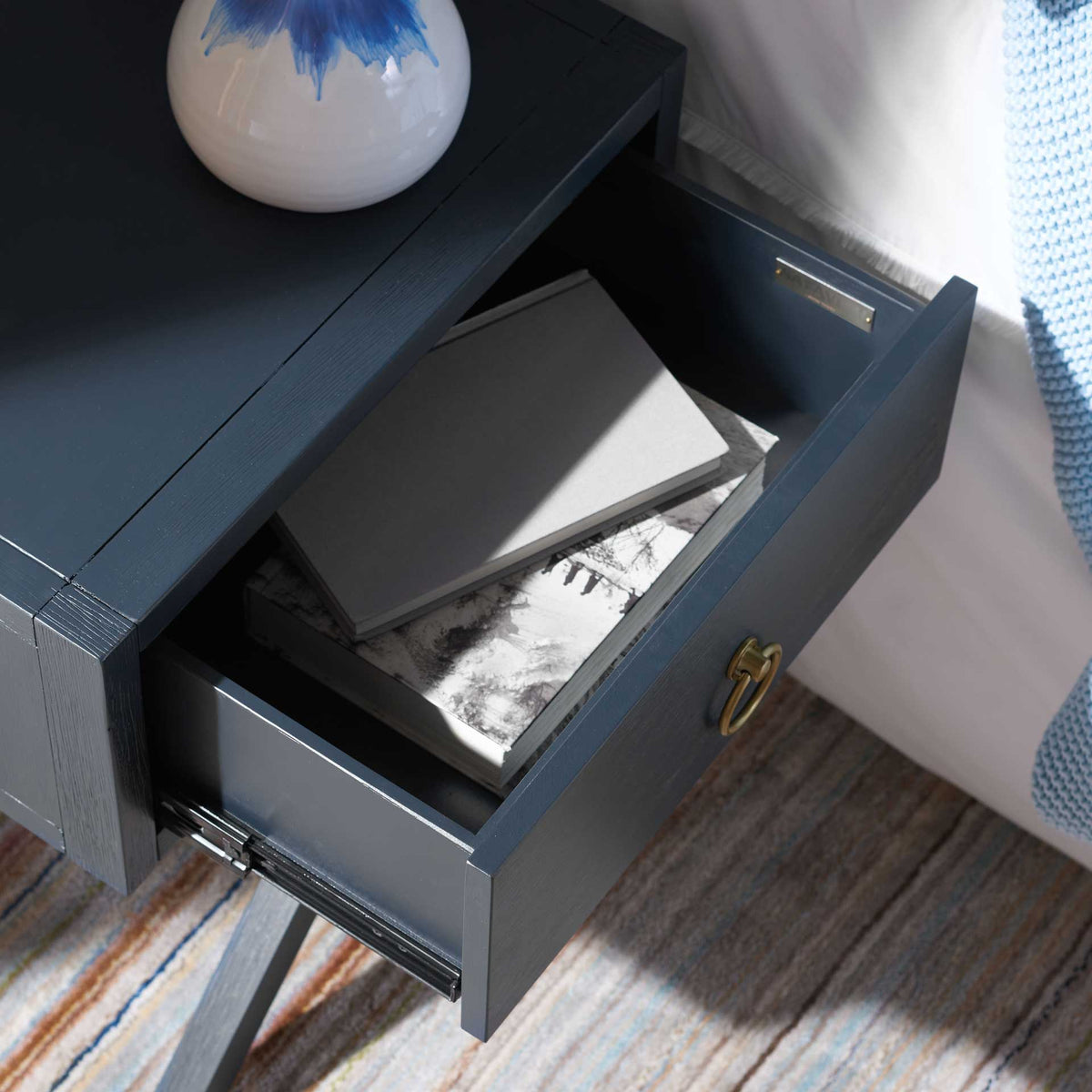 The open navy drawer neatly stores reading material within easy reach of the bed.