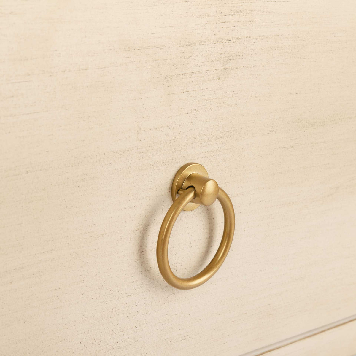 A gold-tone ring pull adds a warm accent to the lightly textured antique white drawer.