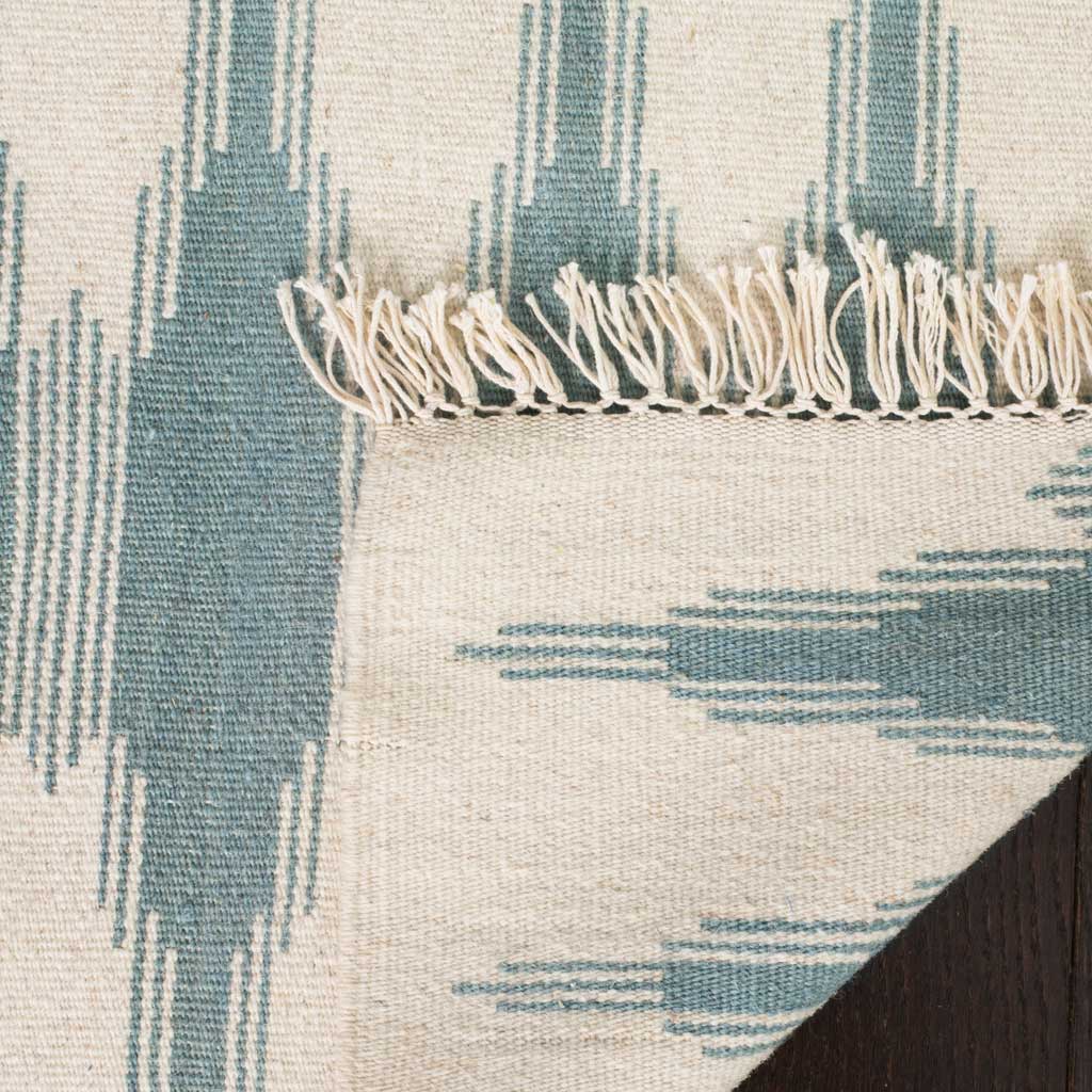 A folded edge reveals the rug's woven reverse, blue pattern, and soft ivory fringe.