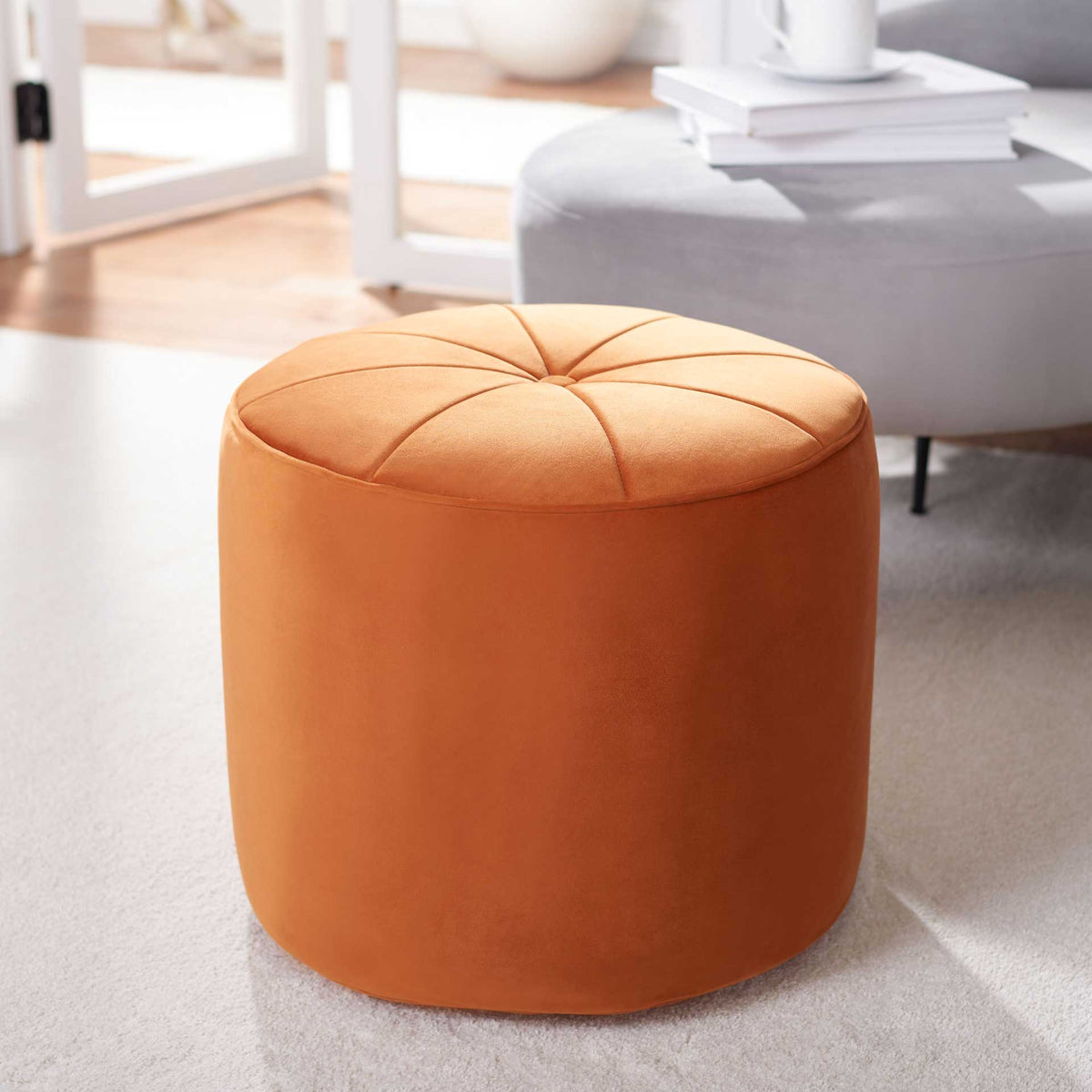 An orange velvet ottoman adds a bold, cozy accent with its round form and plush, tufted seat.