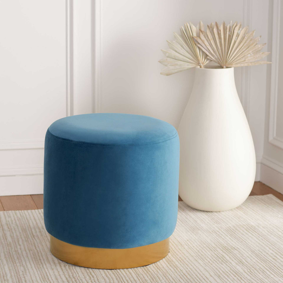 A compact blue velvet ottoman adds a cozy pop of color and a warm gold accent to your space.