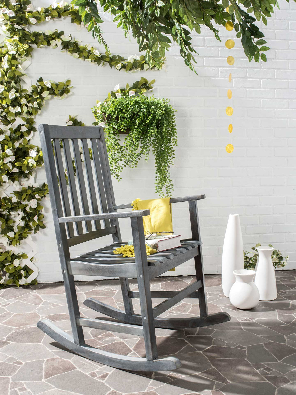 Ash gray rocking chair brings slatted comfort and relaxed, classic style to a leafy patio.