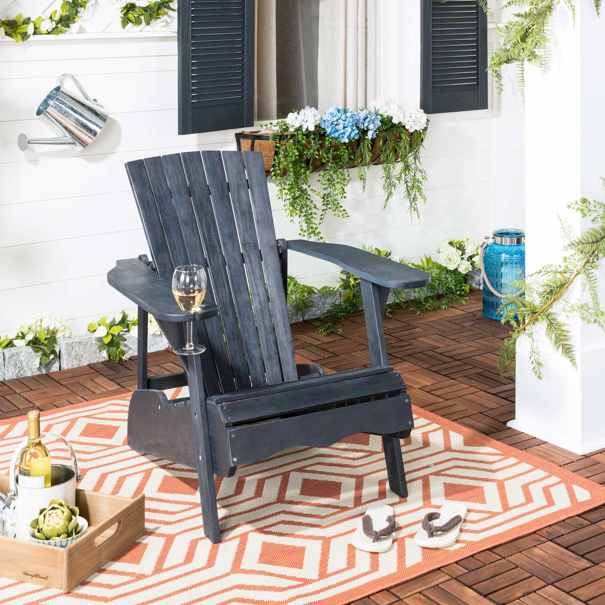 Dark slate gray Adirondack chair with a glass holder rests on a patterned patio rug