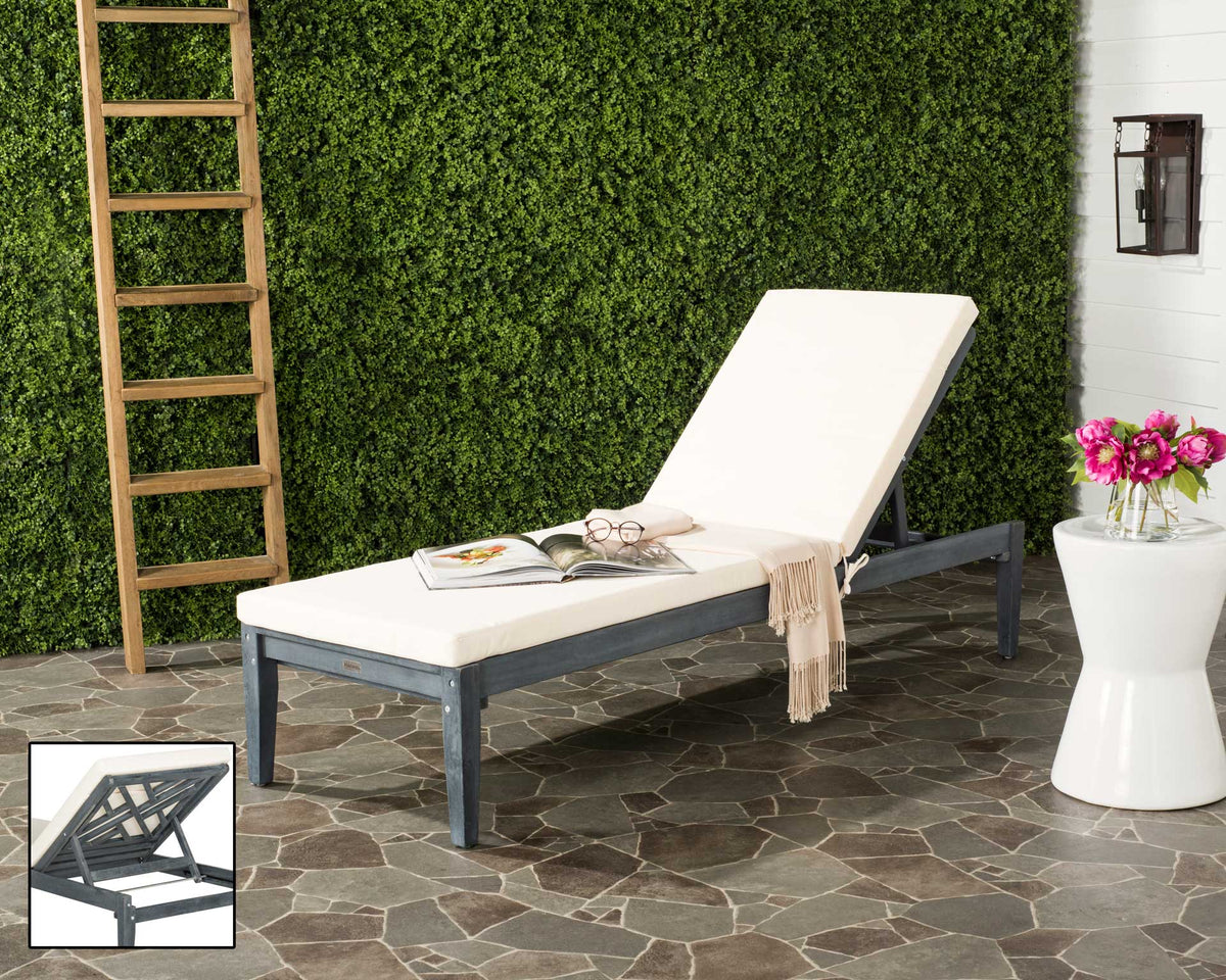 An ash-gray wood chaise with plush beige cushions creates a restful spot on a stone patio.