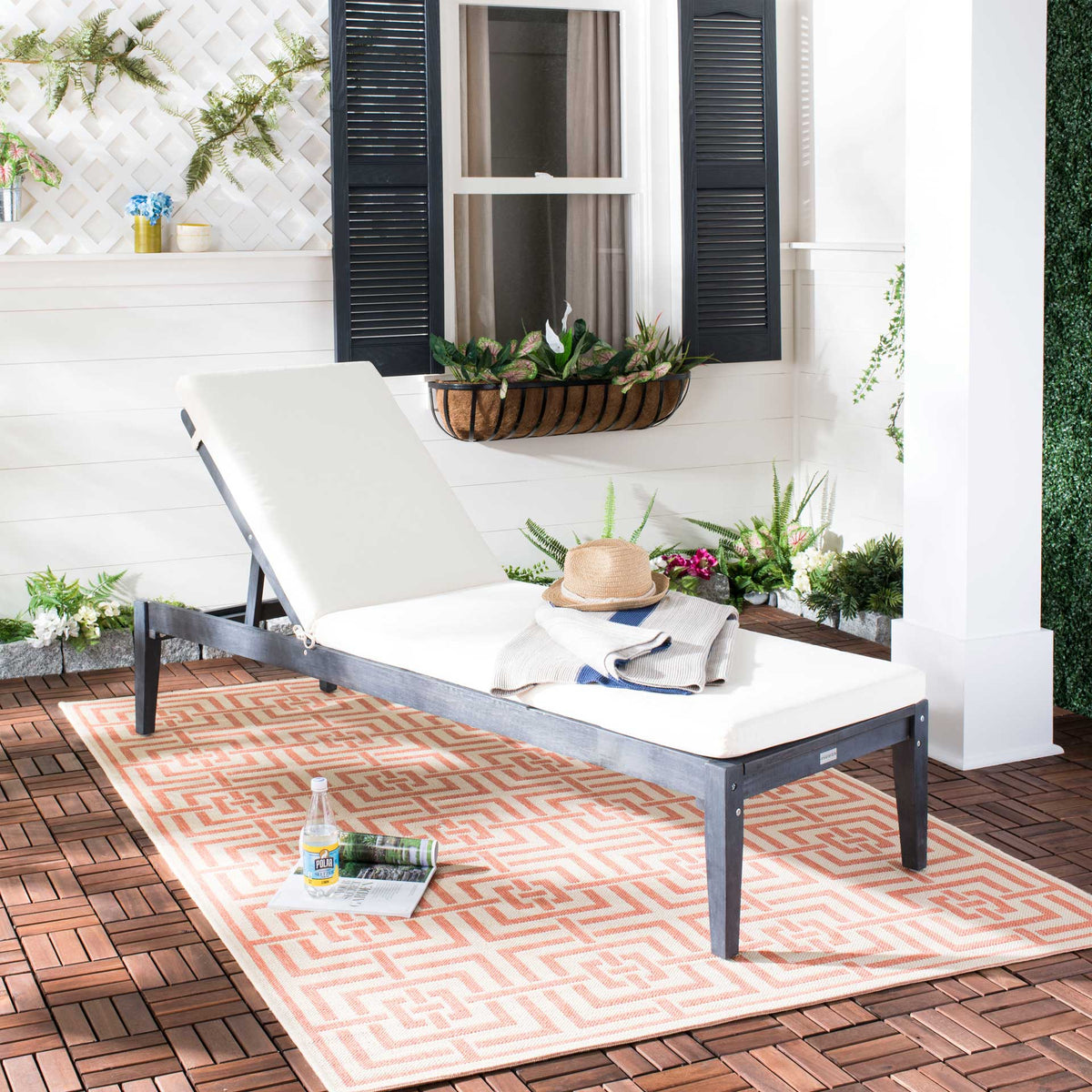 Dark slate gray wood sun lounger and beige cushions bring relaxed comfort to a plant-filled patio