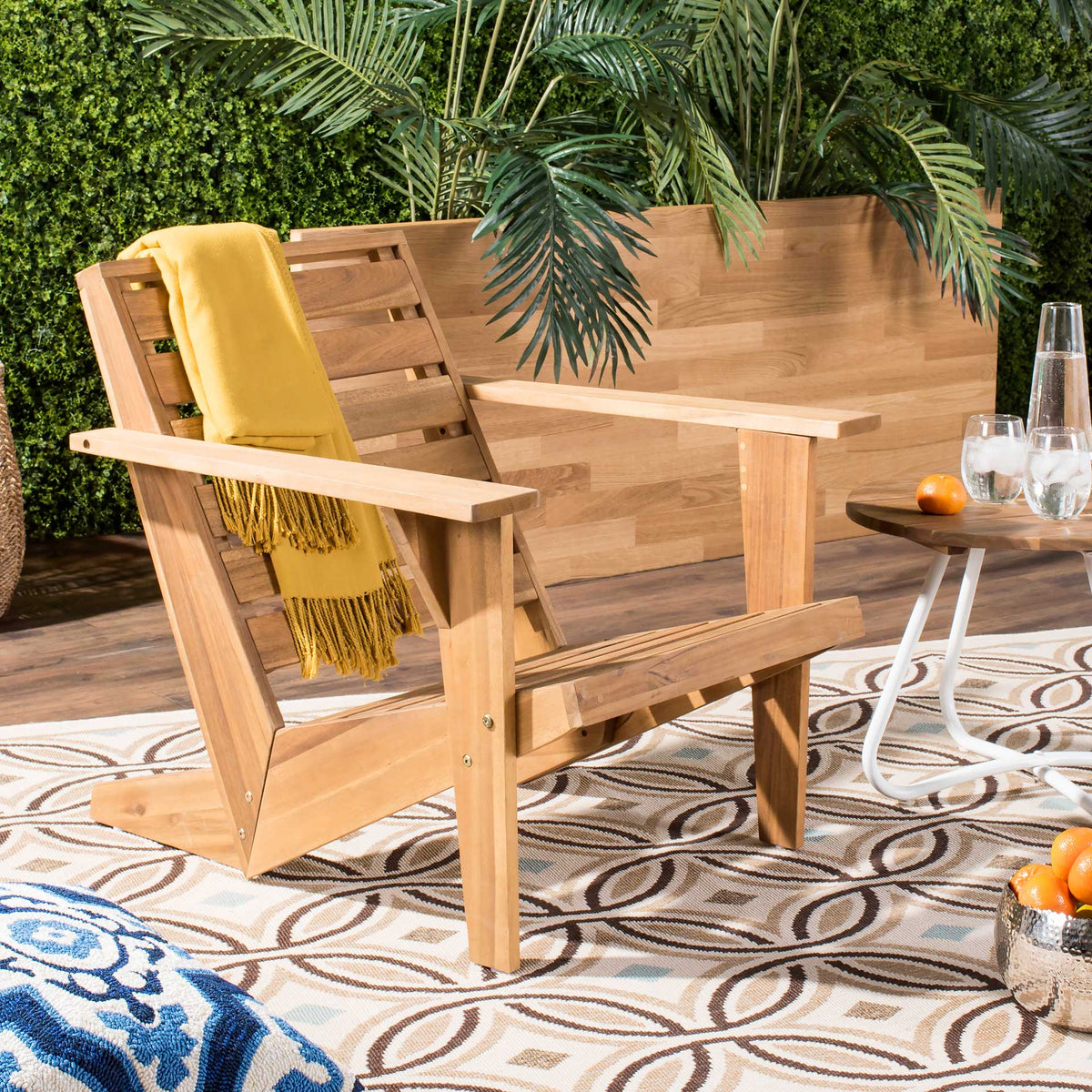 Natural acacia Adirondack chair with a yellow throw, broad arms, and a cozy patio feel