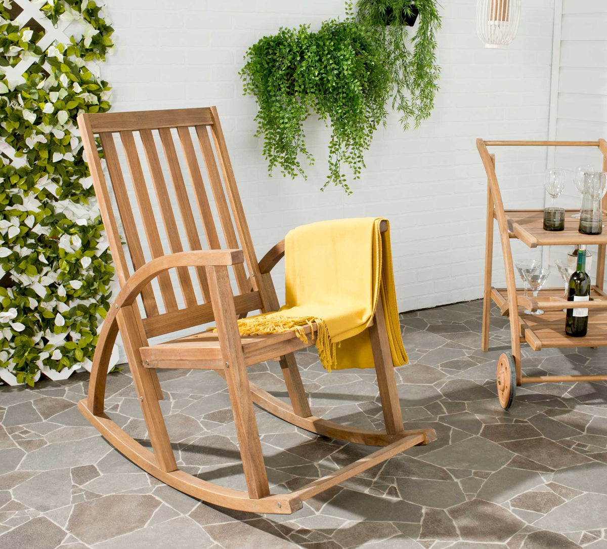 Natural acacia rocker with a slatted back and a yellow throw draped over its curved arm