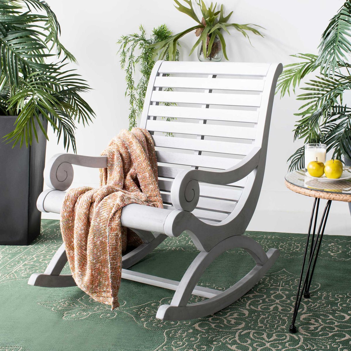 Soft gray scroll arms and a slatted back bring easygoing style to a leafy outdoor retreat