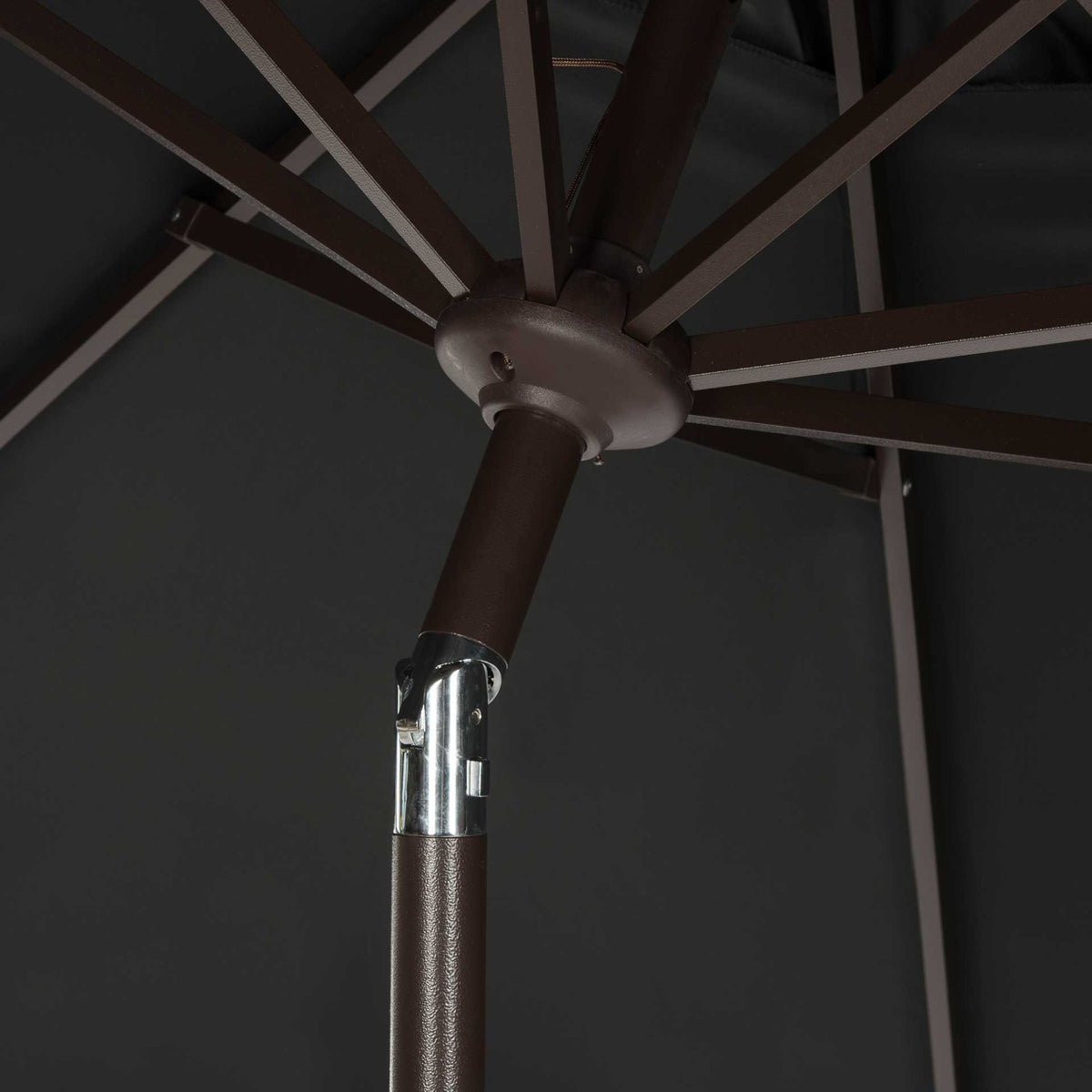 Dark umbrella ribs meet at a central hub above a polished metal tilt joint