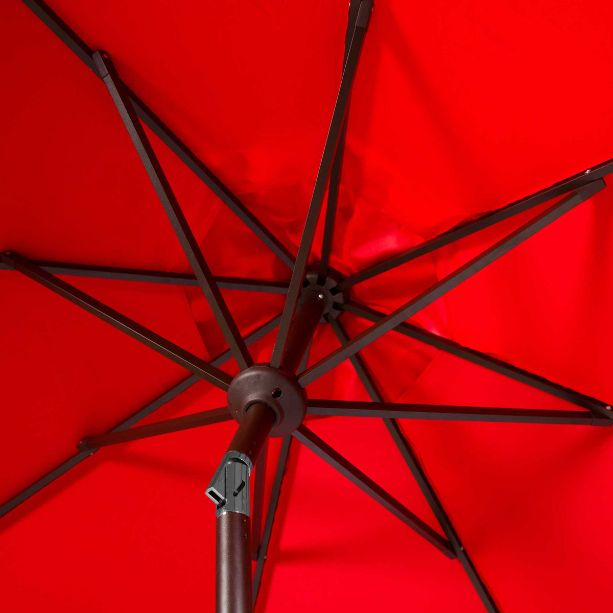 Metal ribs radiate beneath red fabric from a central hub above the hinged brown pole.