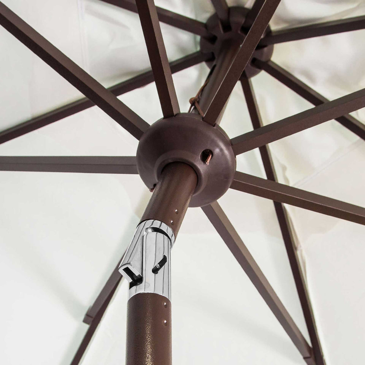 Brown metal ribs meet beneath ivory fabric at a central hub above the silver tilt hinge.