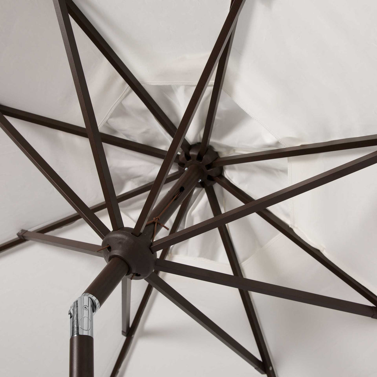 Brown metal ribs converge beneath the ivory canopy at a central hub and tilt joint.