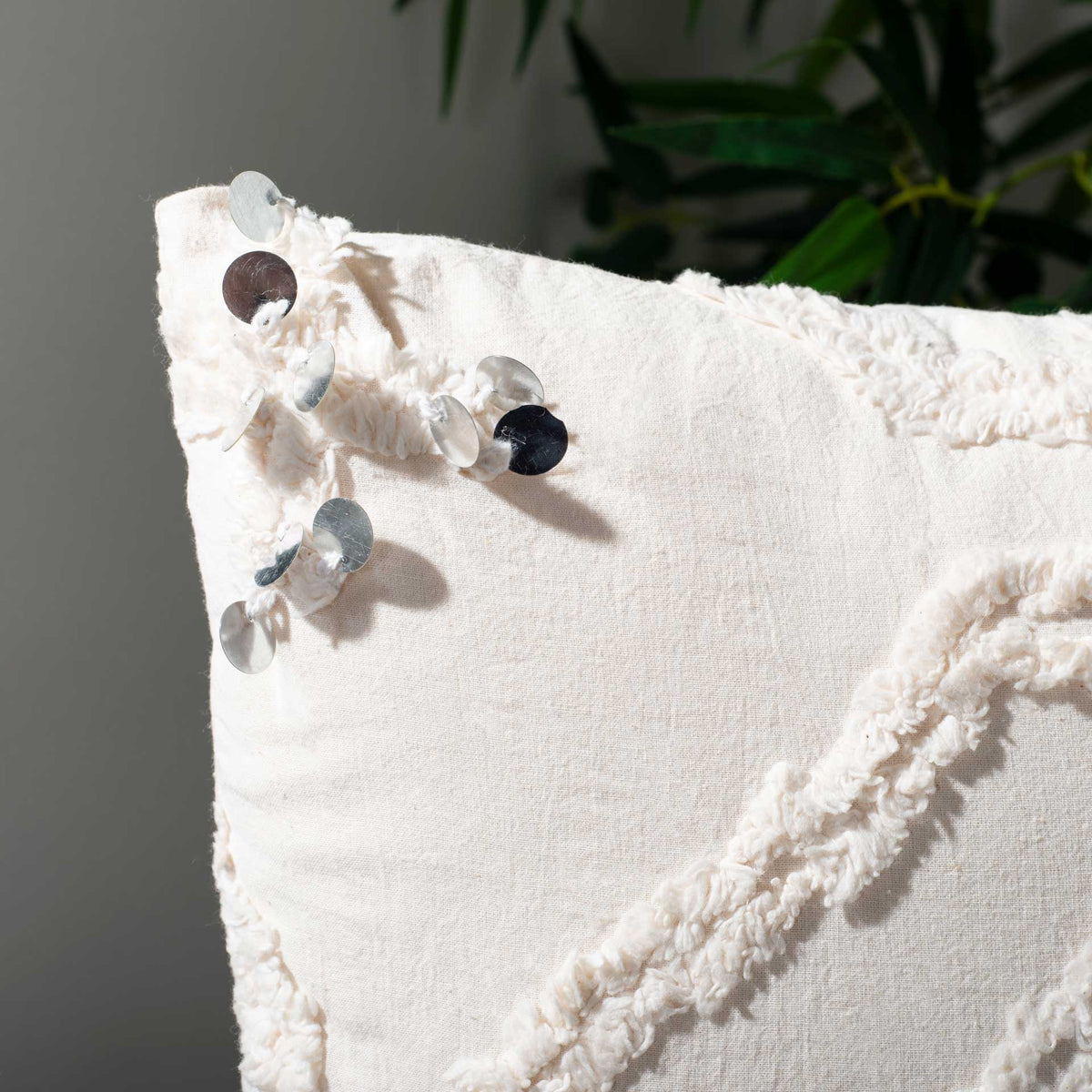 Silver and black sequins dangle beside raised ivory tufting on this white accent pillow
