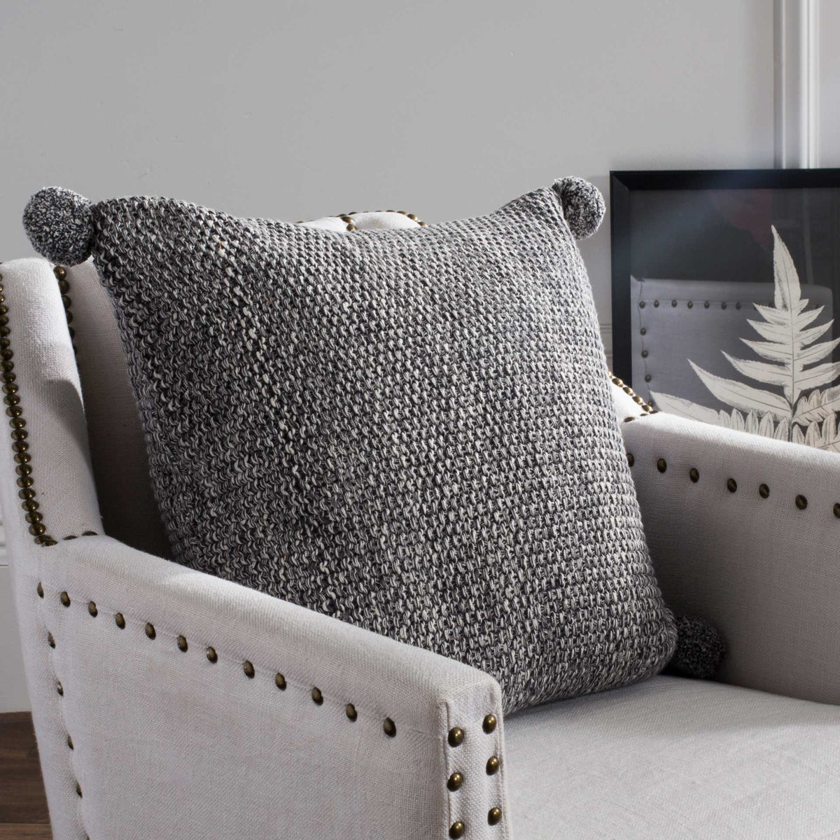 A square gray knit pillow with pom-pom accents adds cozy texture to a neutral armchair.