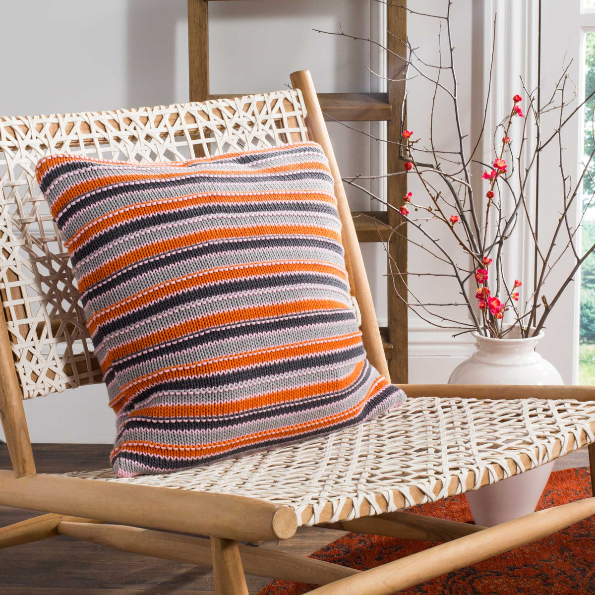 An orange, pink, and charcoal striped pillow brings cozy color to a woven accent chair.