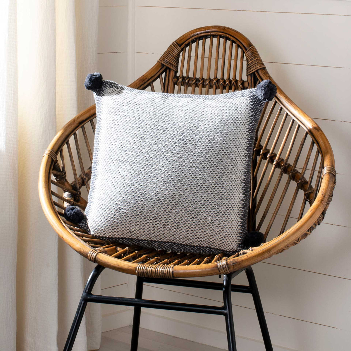 Square knit pillow softens a woven chair with neutral tones and charcoal pom-pom corners