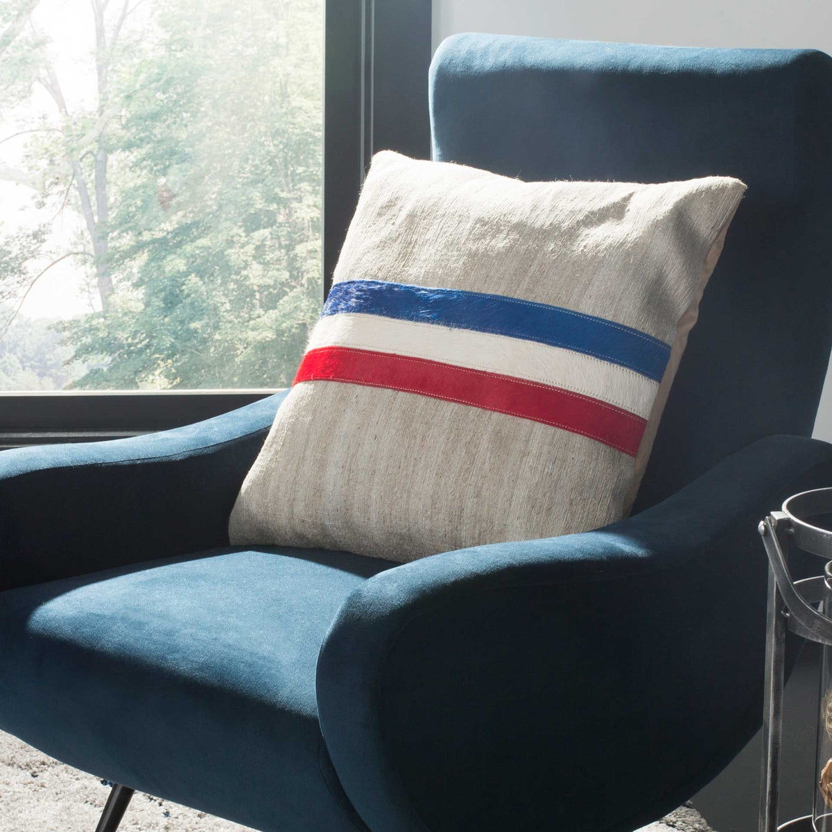 Gray accent pillow brings vivid blue, white, and red bands to a plush navy armchair
