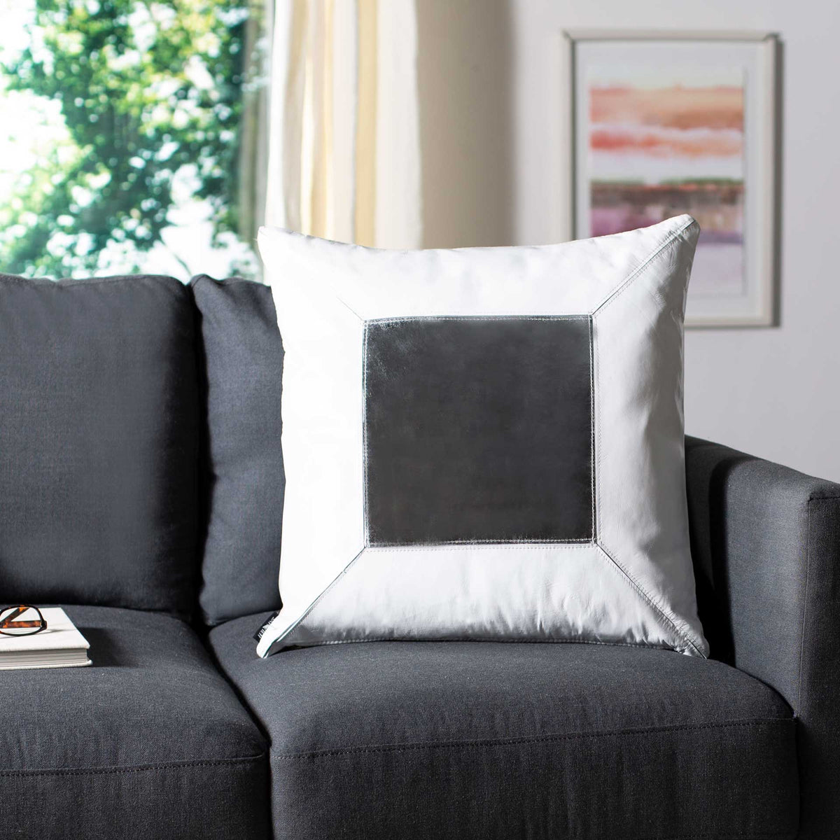 A white pillow with a lustrous silver inset adds bold contrast to a charcoal sofa
