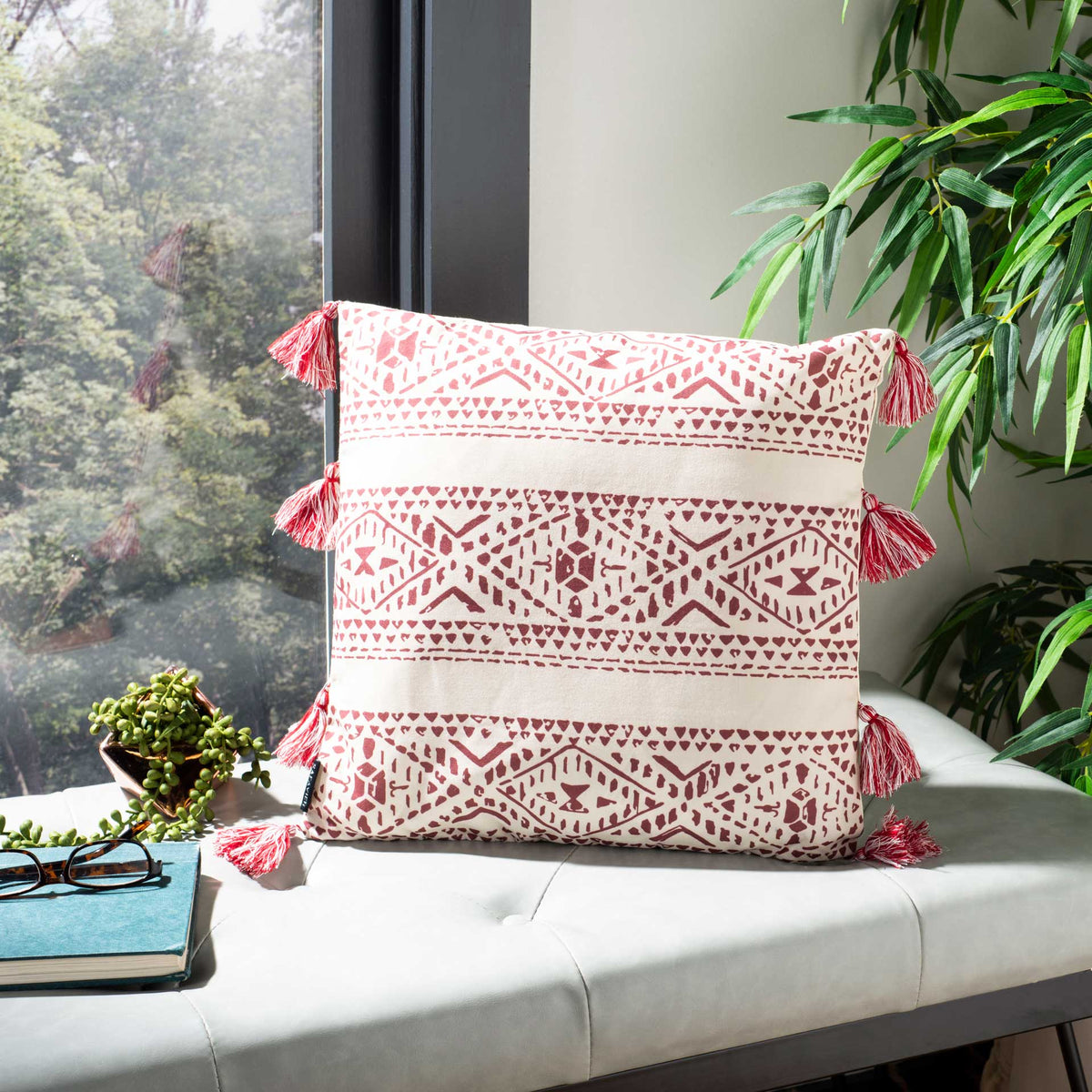 Red geometric stripes and tassels brighten a beige pillow on an upholstered bench