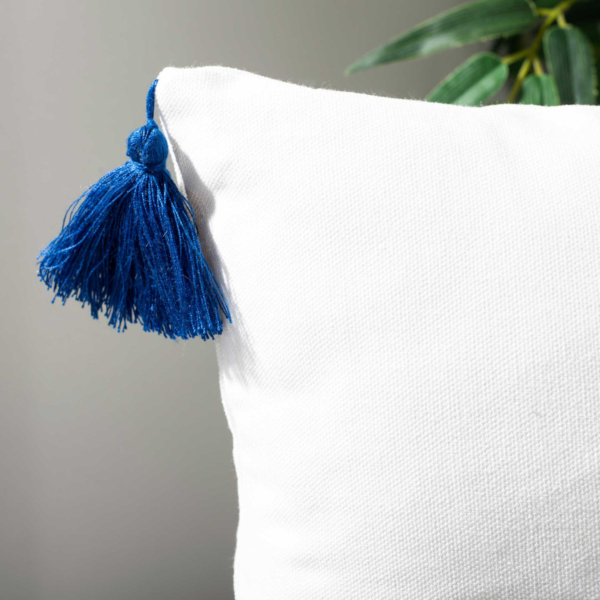 A navy corner tassel adds playful texture to the white woven pillow cover