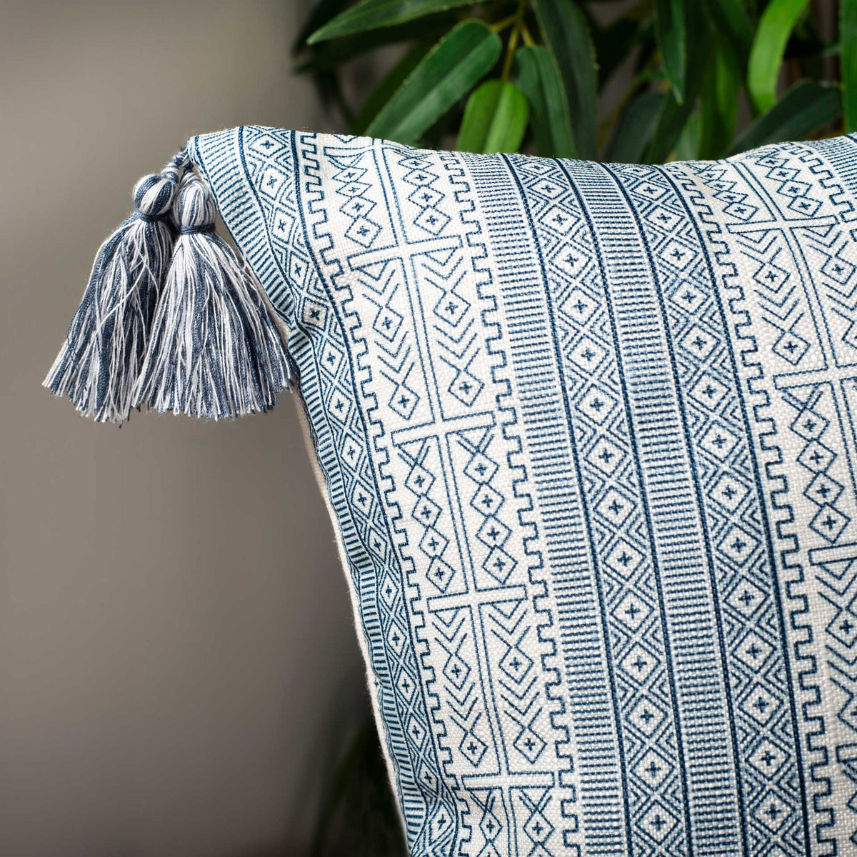 A corner tassel and intricate blue geometric bands add playful texture to the white pillow.