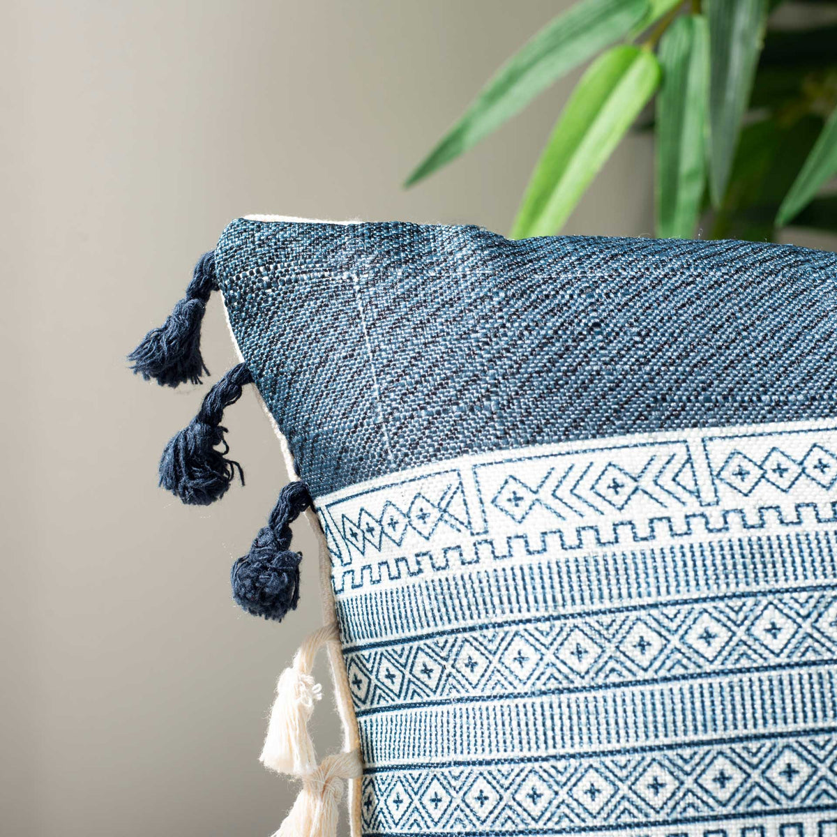 Textured navy fabric frames fine blue geometric bands and soft cream and navy tassels.