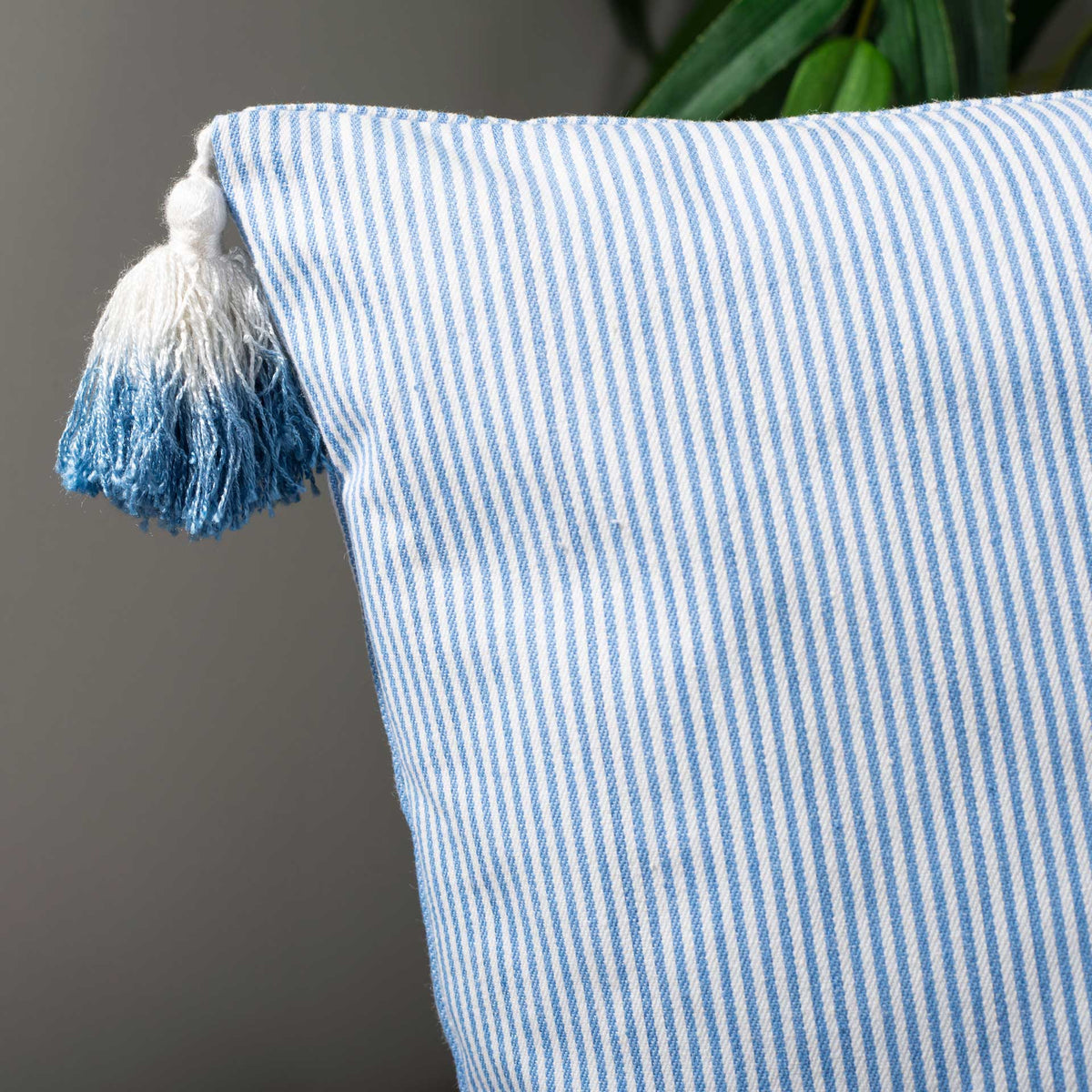Blue-and-white tassels add playful texture to the pillow's finely striped cotton cover.