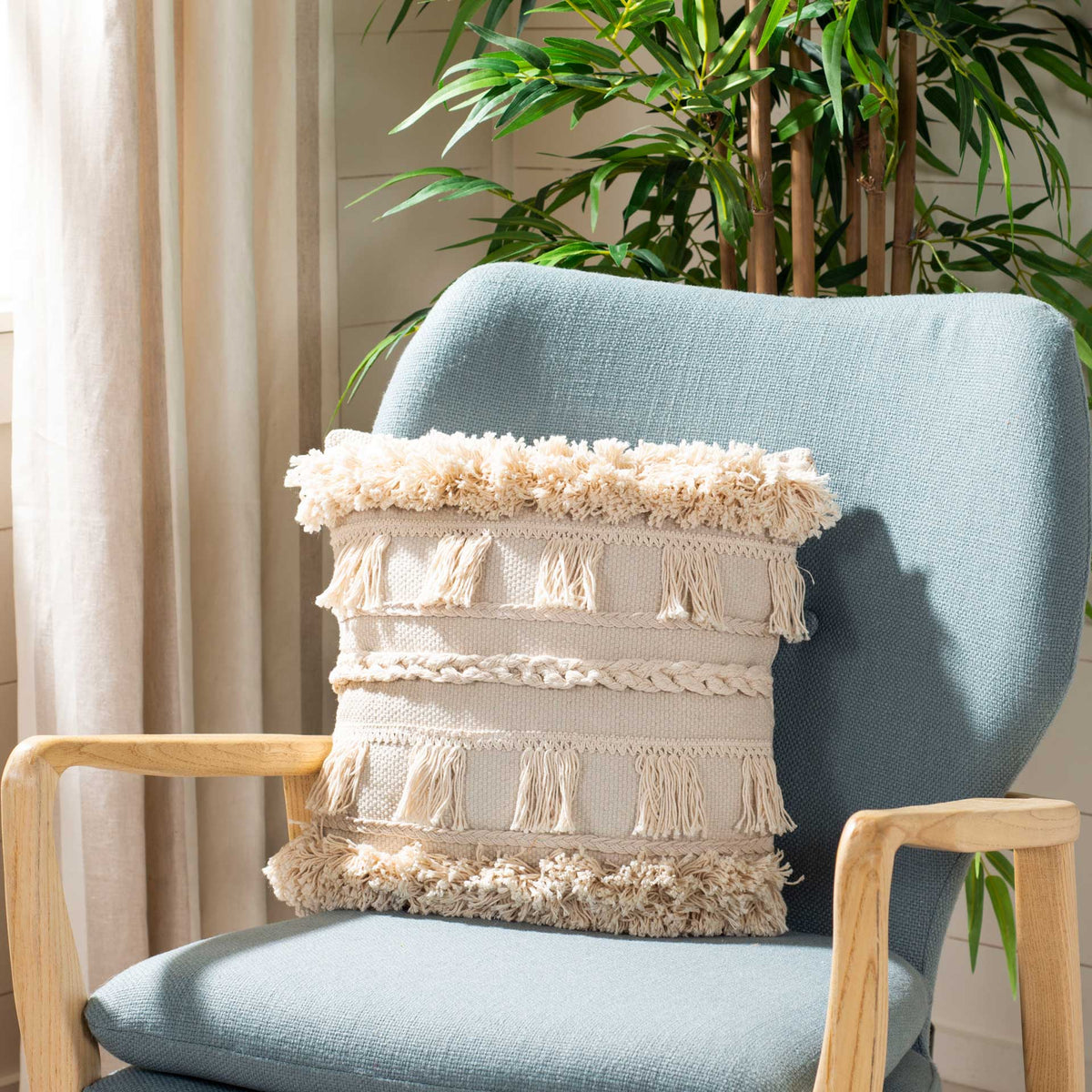Layered tassels and fluffy fringe give this beige pillow cozy contrast against a blue chair.