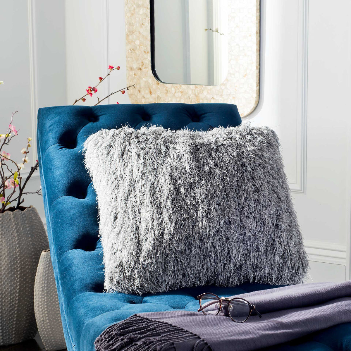 A fluffy white shag pillow brightens a deep blue tufted chair with inviting texture.