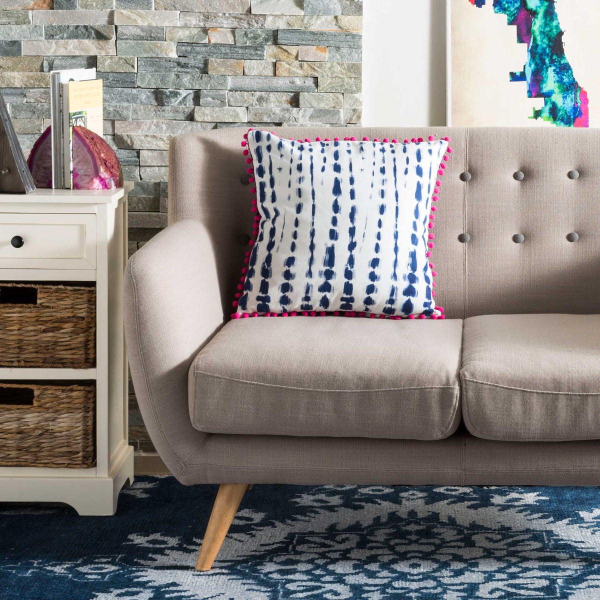 Navy brushstroke stripes and pink pom-pom edging enliven this cream pillow on a neutral sofa